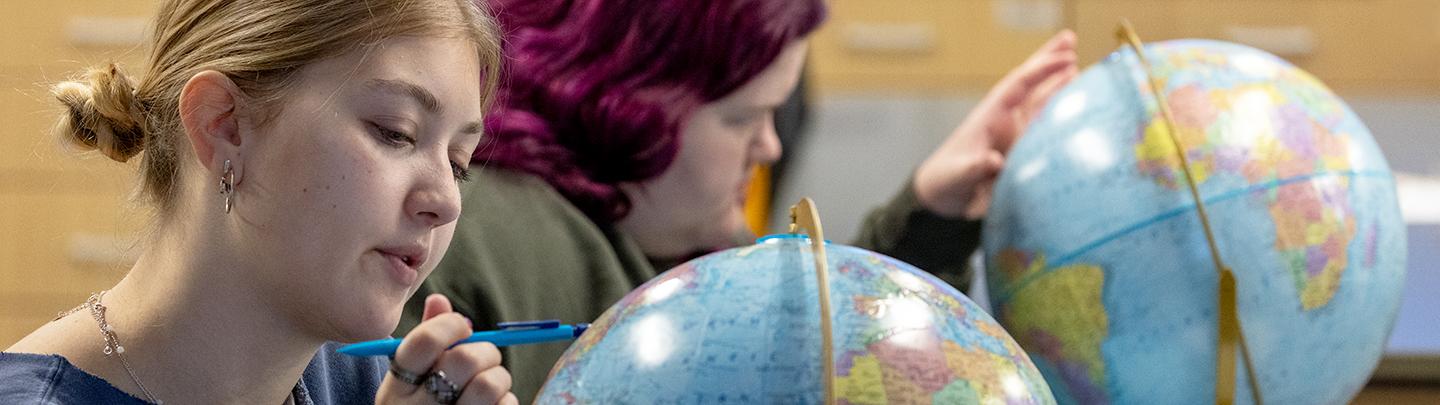 student pointing at spot on globe